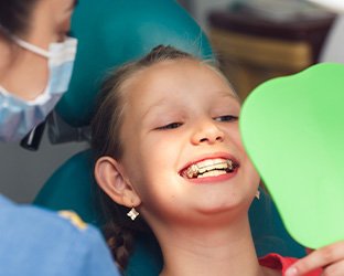 a young patient with a retainer looking in a handheld mirror in a dental office