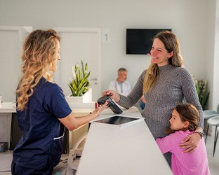 a parent paying at a dental office with her child at her side