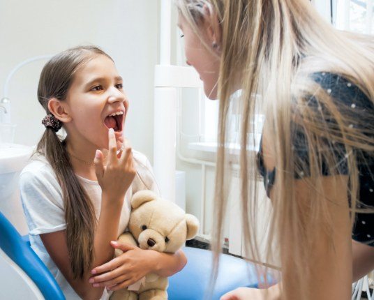 Child in dental chair pointing to smile