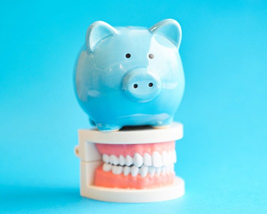 Piggy bank atop model teeth representing the cost of pediatric dental emergencies