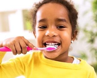 Young girl in yellow sweater brushing her teeth
