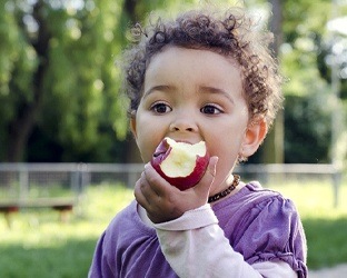 Little boy eating an apply outside