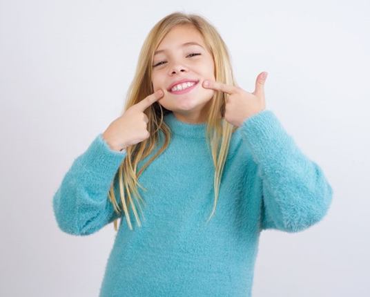 Smiling child pointing at her teeth