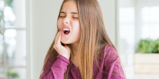 Child in need of emergency dentistry holding cheek in pain