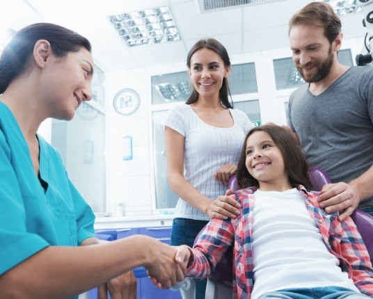 Young girl shaking dentist's hand during dental checkup and teeth cleaning visit