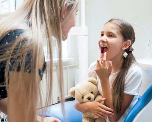 Young girl pointing to smiles after dental sealant treatment