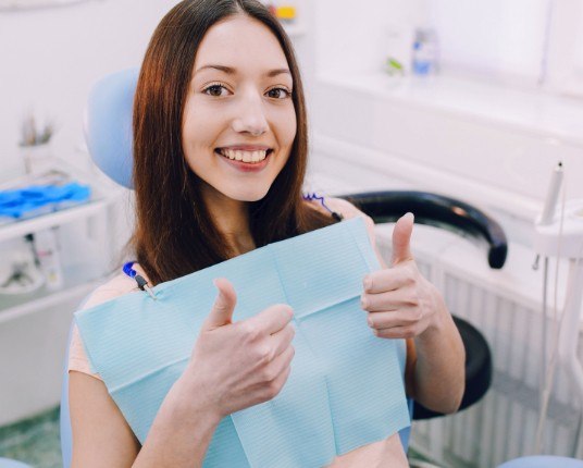 Young woman in dental chair giving thumbs up during dentistry for teens visit