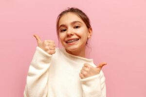 Child with braces smiling and holding two thumbs up